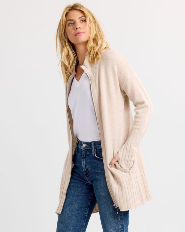 Three-quarter view image of a woman wearing oatmeal zip-up cashmere cardigan with pockets over white top and jeans