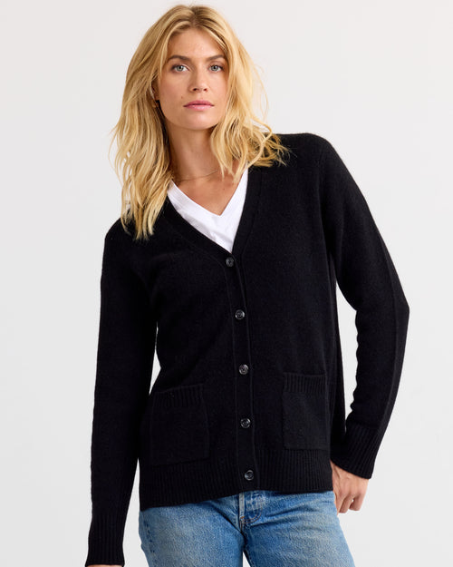 LIFESTYLE / EDITORIAL: Woman wearing black buttoned cashmere cardigan over white V-neck shirt and blue jeans against white