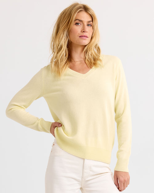 Front angled image of a woman wearing a buttermilk yellow V-neck cashmere sweater with white pants