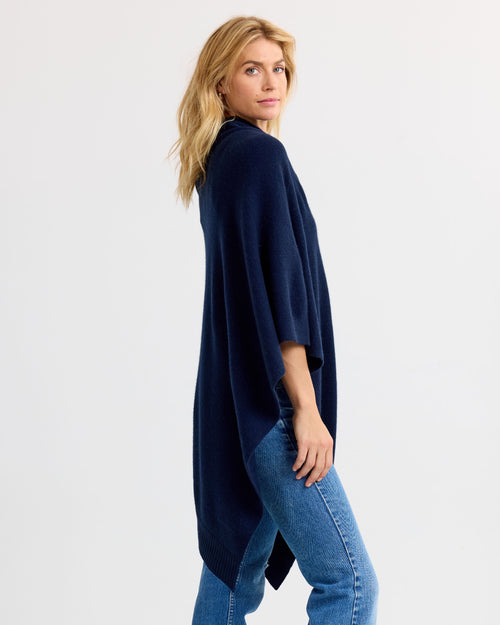 LIFESTYLE / EDITORIAL: Woman wearing navy cashmere cardigan and blue jeans, posing sideways against white background