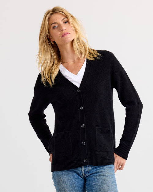 LIFESTYLE / EDITORIAL: Woman wearing black cashmere cardigan over white V-neck shirt and blue jeans against plain background