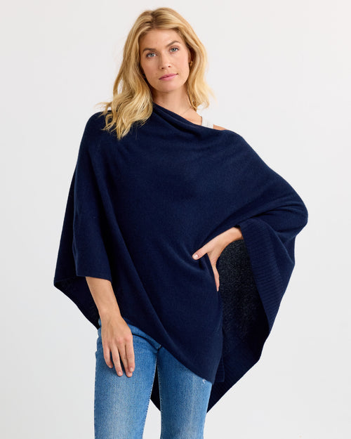 LIFESTYLE / EDITORIAL: Woman wearing navy cashmere poncho over white top and jeans against white background