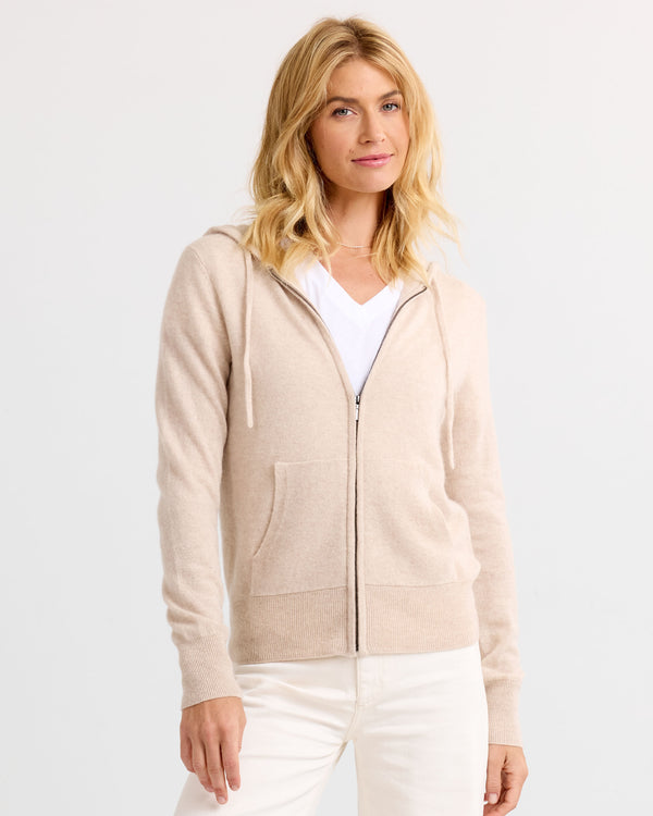 LIFESTYLE / EDITORIAL: Woman wearing oatmeal zip-up cashmere hoodie and white pants against plain background