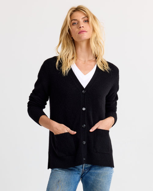 Front view image of a woman wearing a black buttoned cashmere cardigan with pockets over a white top and blue jeans