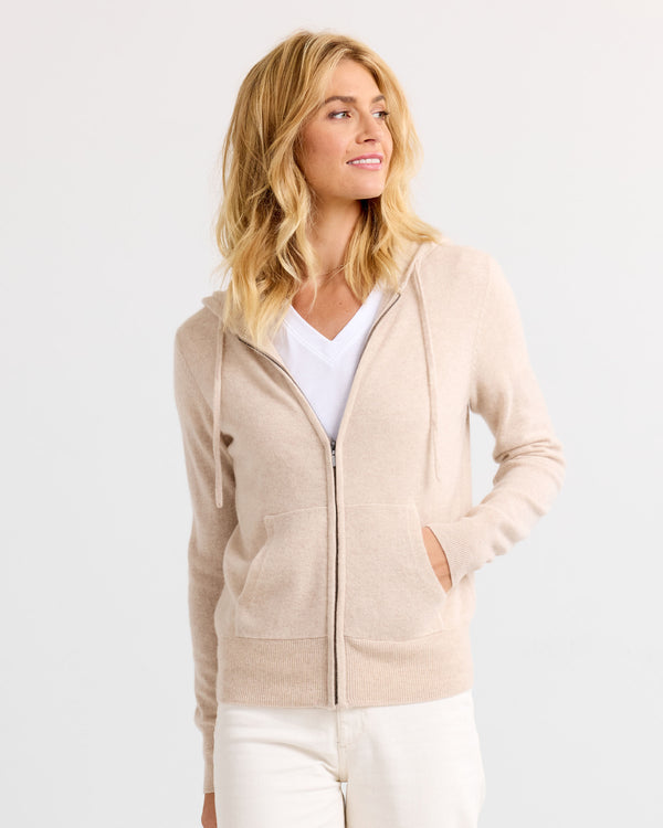 LIFESTYLE / EDITORIAL: Woman wearing oatmeal zip-up cashmere hoodie and white pants, looking to side against white background