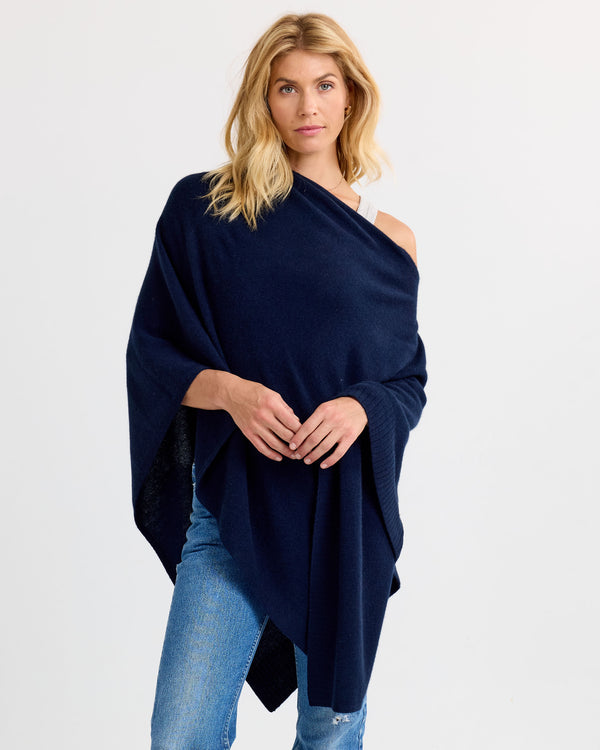 LIFESTYLE / EDITORIAL: Woman wearing navy cashmere wrap over white top and jeans against plain background