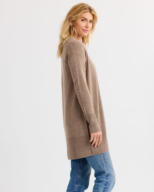 LIFESTYLE / EDITORIAL: Woman in driftwood-colored long cashmere sweater and blue jeans, posing sideways against white