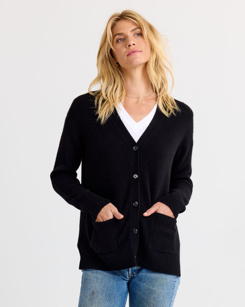 LIFESTYLE / EDITORIAL: Woman wearing black cashmere cardigan over white top and jeans against plain background