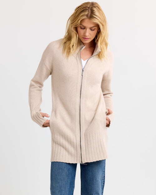 LIFESTYLE / EDITORIAL: Woman wearing long oatmeal zip-up cashmere cardigan with pockets and blue jeans against white