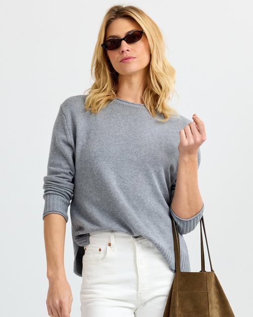 LIFESTYLE / EDITORIAL: Woman in gray cashmere sweater, white pants, sunglasses, holding brown suede tote bag against white
