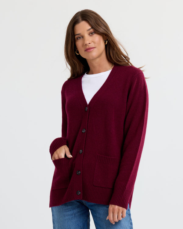 LIFESTYLE / EDITORIAL: Woman wearing a cabernet-colored cashmere cardigan over a white top and blue jeans against white