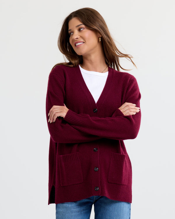 LIFESTYLE / EDITORIAL: Woman wearing a cabernet-colored cashmere cardigan over a white top and blue jeans, smiling with arms
