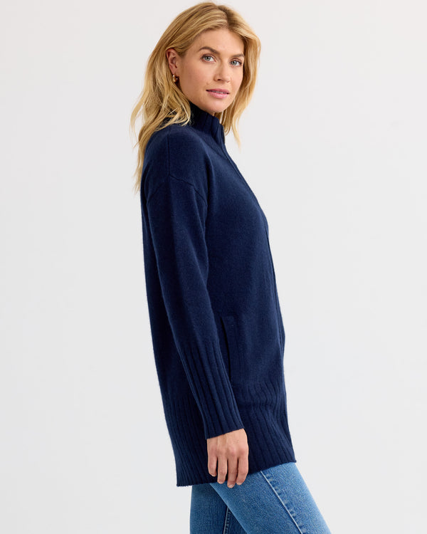 Side profile image of a woman wearing a navy blue long cashmere sweater with jeans against a white background