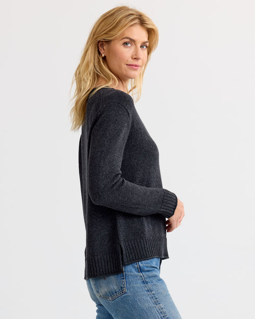 LIFESTYLE / EDITORIAL: Woman wearing charcoal cashmere sweater and blue jeans, standing sideways against white background
