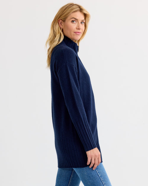 LIFESTYLE / EDITORIAL: Woman wearing navy blue long cashmere sweater and jeans, standing sideways against white background