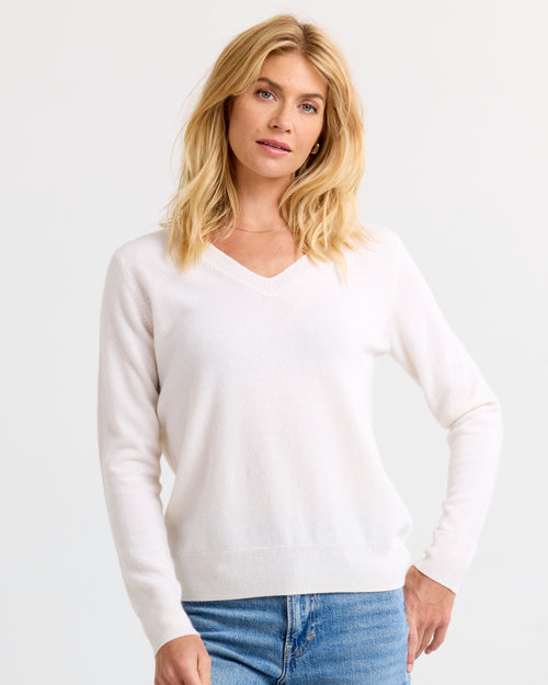 LIFESTYLE / EDITORIAL: Woman wearing ivory V-neck cashmere sweater and blue jeans against a plain background