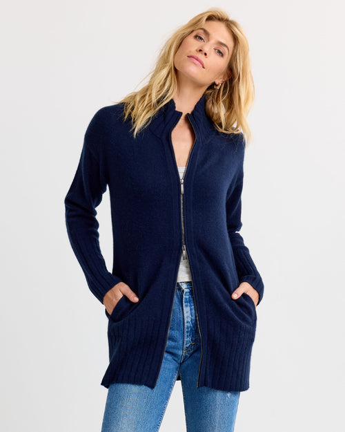 LIFESTYLE / EDITORIAL: Woman wearing navy zip-up cashmere cardigan with pockets and blue jeans against white background