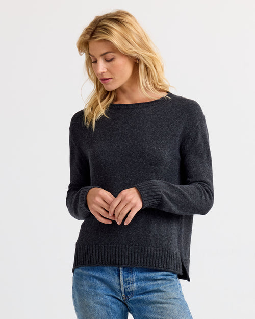 Front three-quarter view image of a woman wearing a charcoal cashmere sweater and blue jeans, looking down.