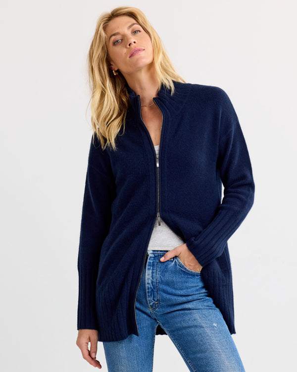 Front-facing image of a woman wearing a navy zip-up cashmere cardigan with jeans, posing confidently against plain background