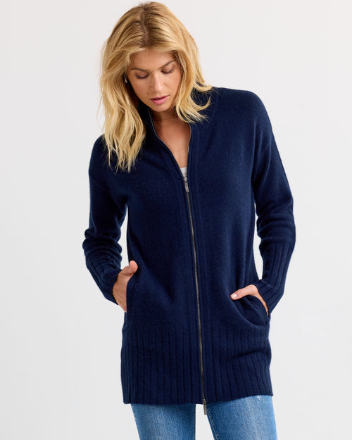 Woman wearing navy zip-up long cashmere cardigan with pockets, standing against plain light background