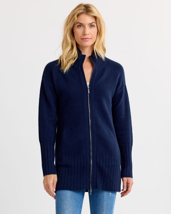 LIFESTYLE / EDITORIAL: Woman wearing navy zip-up cashmere cardigan and jeans, standing against a plain white background