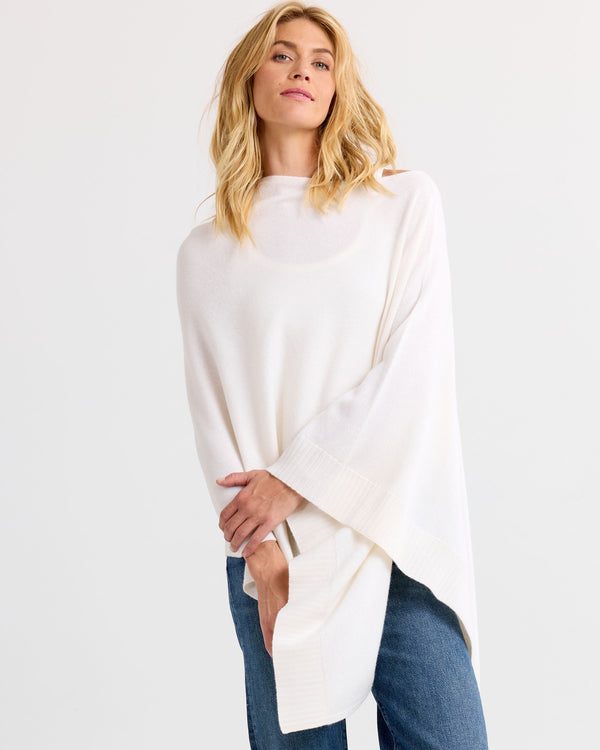 LIFESTYLE / EDITORIAL: Woman wearing ivory cashmere poncho with blue jeans against white background