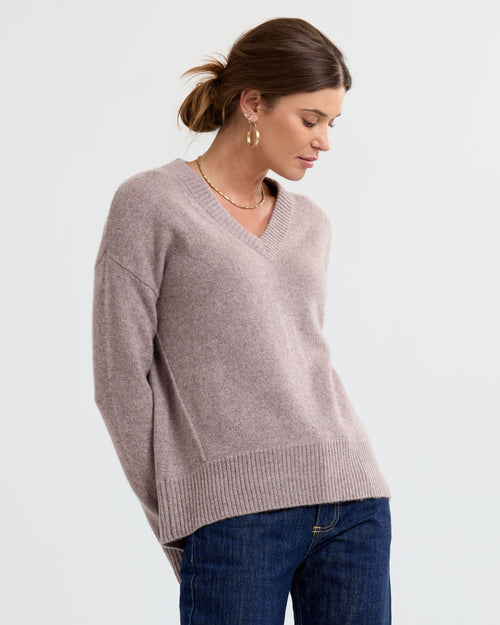 LIFESTYLE / EDITORIAL: Woman wearing a latte-colored V-neck cashmere sweater and jeans, looking down to the side