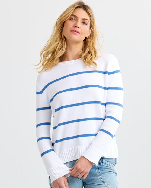 Three-quarter view image of a woman wearing a white cashmere sweater with blue stripes and light blue jeans