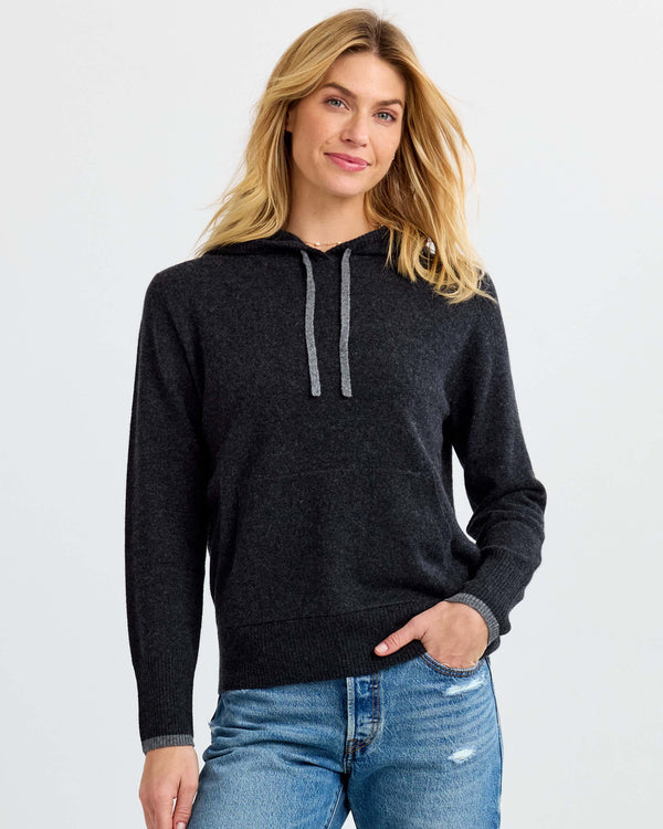 Woman wearing charcoal gray cashmere hoodie sweater with gray drawstrings and blue jeans against white background