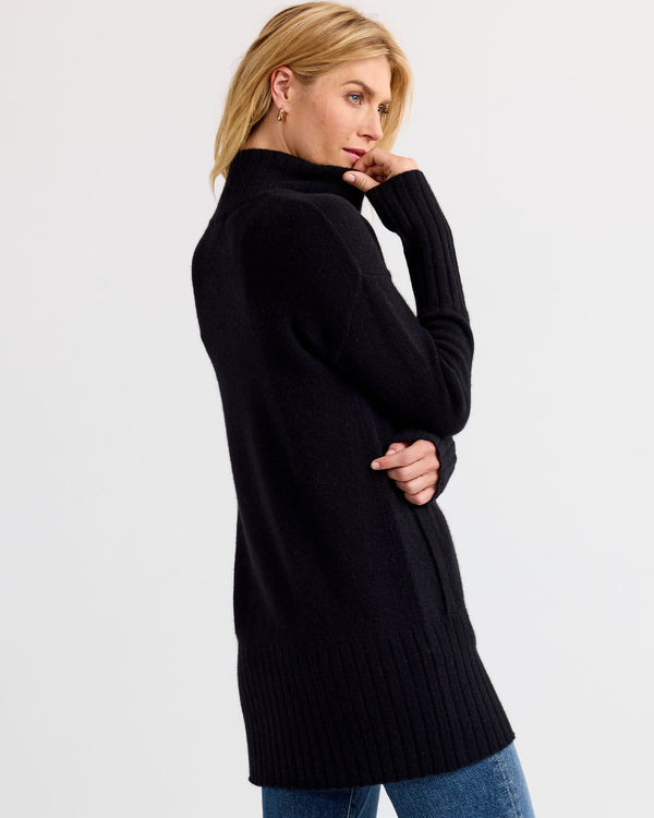 LIFESTYLE / EDITORIAL: Woman wearing long black cashmere sweater, side pose, light background, blue jeans