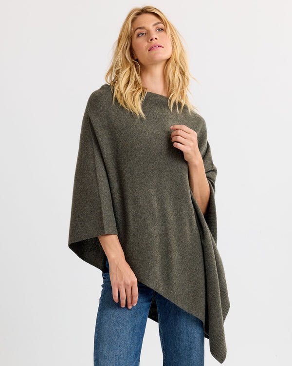 LIFESTYLE / EDITORIAL: Woman wearing dark olive asymmetrical cashmere poncho with jeans against white background