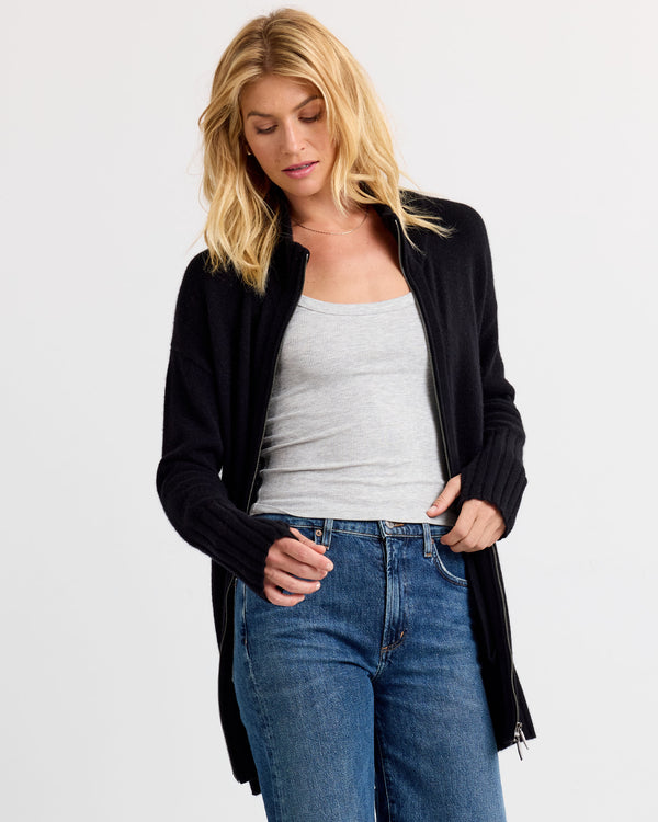LIFESTYLE / EDITORIAL: Woman wearing black zip-up cashmere cardigan, gray tank top, and blue jeans against white background