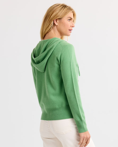 LIFESTYLE / EDITORIAL: Woman wearing a green cashmere hoodie, viewed from the back against a plain background