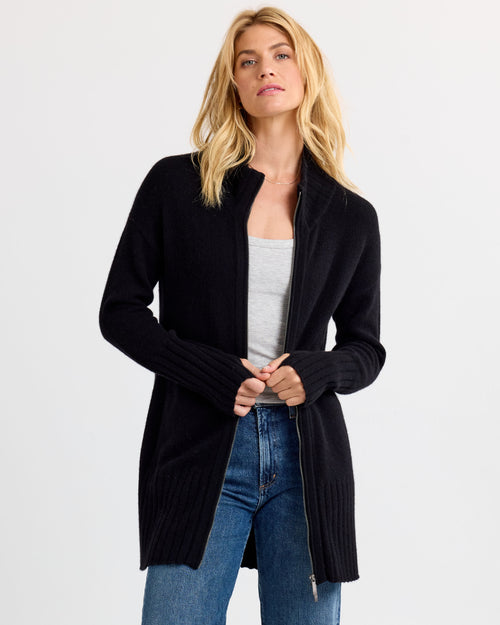 LIFESTYLE / EDITORIAL: Woman wearing black long zip-up cashmere cardigan over gray top and blue jeans against white