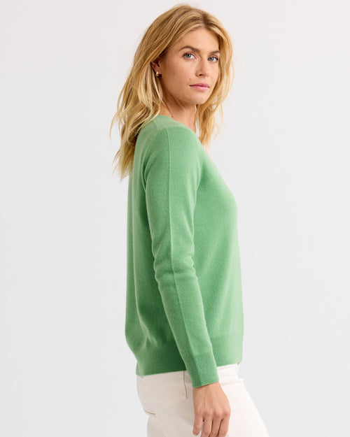 Woman wearing matcha green cashmere sweater, side view, white pants, plain light background