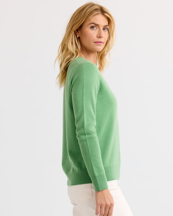 Woman wearing matcha green cashmere sweater, side view, white pants, plain light background
