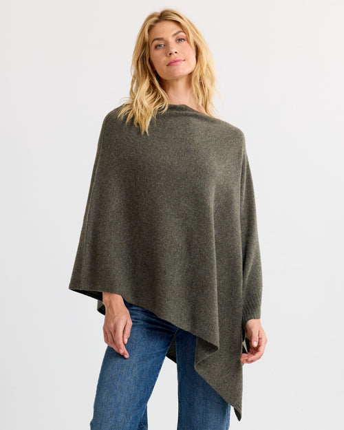 LIFESTYLE / EDITORIAL: Woman wearing dark olive asymmetrical cashmere poncho with blue jeans against white background
