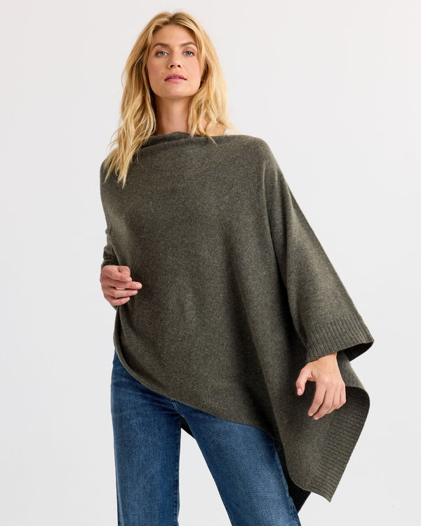 LIFESTYLE / EDITORIAL: Woman wearing dark olive cashmere poncho with jeans against white background