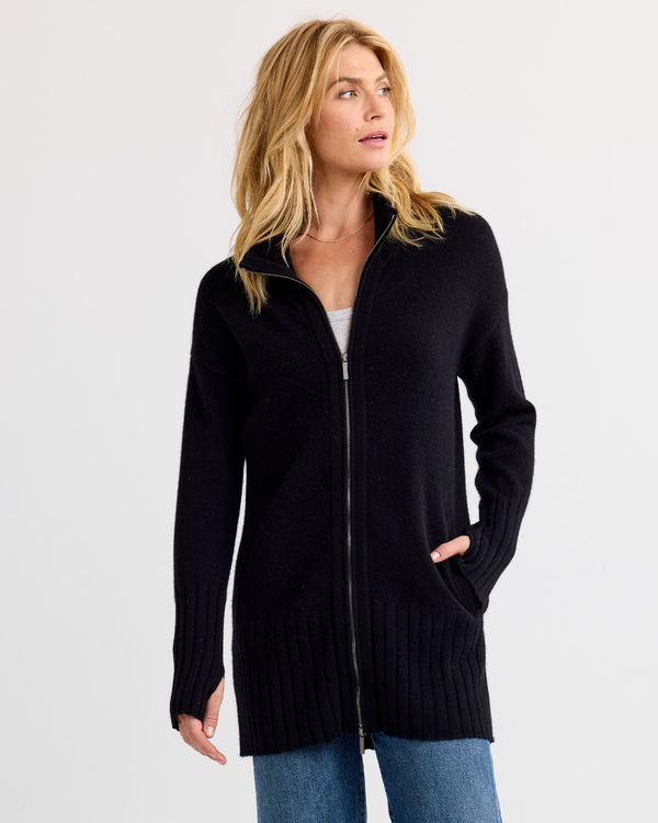 LIFESTYLE / EDITORIAL: Woman wearing long black zip-up cashmere cardigan with pockets and blue jeans, looking to side