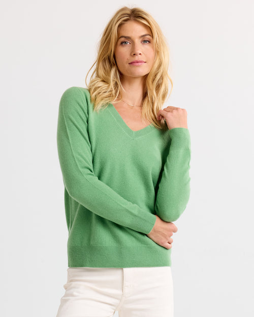 LIFESTYLE / EDITORIAL: Woman wearing a matcha green V-neck cashmere sweater and white pants against a plain background
