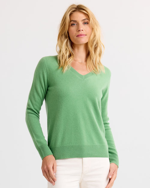 Woman wearing matcha green V-neck cashmere sweater and white pants, standing against white background