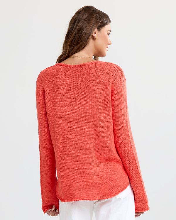 LIFESTYLE / EDITORIAL: Woman wearing coral cashmere sweater, viewed from back, paired with white pants against white