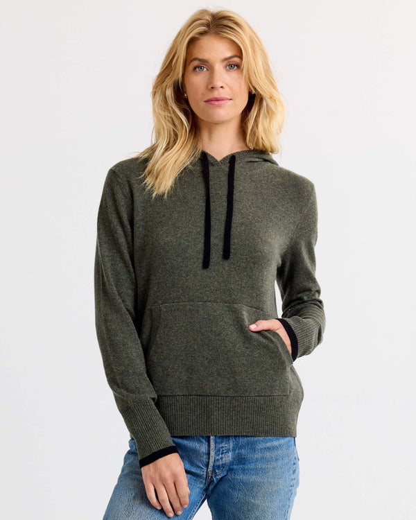 LIFESTYLE / EDITORIAL: Woman wearing dark olive cashmere hoodie with black drawstrings and blue jeans against white