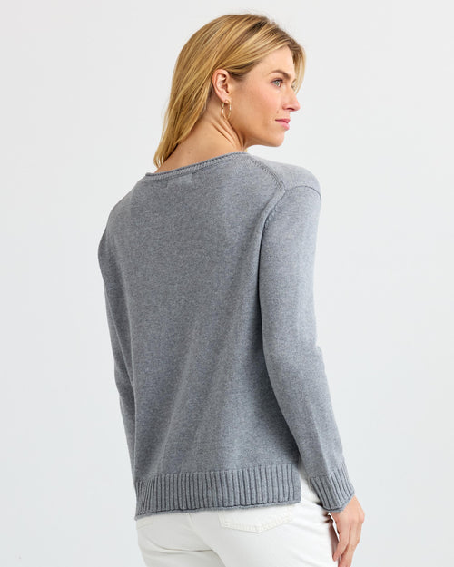 LIFESTYLE / EDITORIAL: Woman wearing grey cashmere sweater, facing away, with white pants against plain background