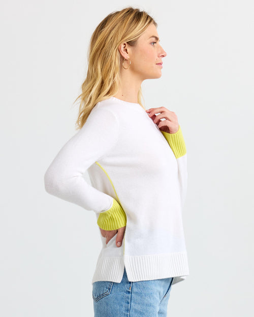 LIFESTYLE / EDITORIAL: Woman in white cashmere sweater with yellow cuffs, side profile, against plain background