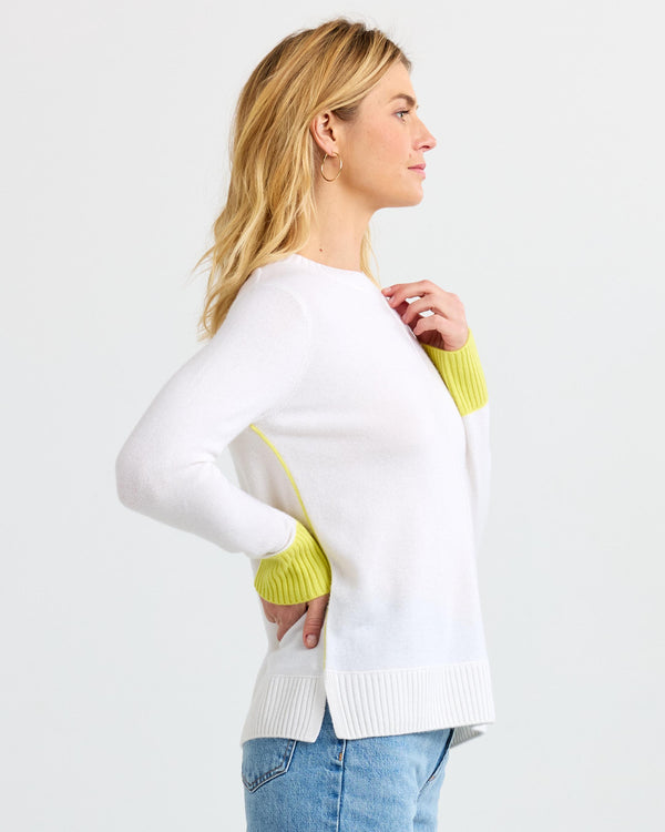 LIFESTYLE / EDITORIAL: Woman in white cashmere sweater with yellow cuffs, side profile, against plain background