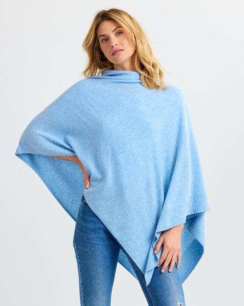 LIFESTYLE / EDITORIAL: Woman wearing light blue cashmere poncho and jeans against plain white background
