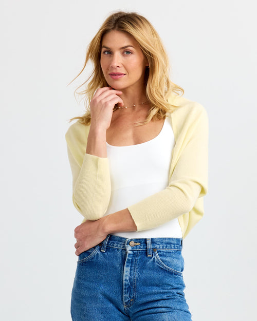 LIFESTYLE / EDITORIAL: Woman wearing buttermilk yellow cashmere shrug over white top and blue jeans against white background
