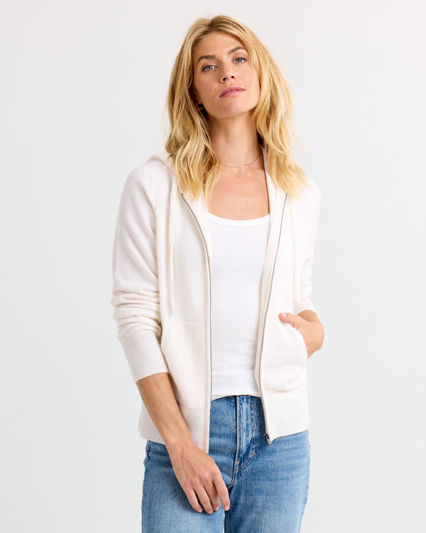 LIFESTYLE / EDITORIAL: Woman wearing ivory zip-up cashmere hoodie over white tank and blue jeans against white background