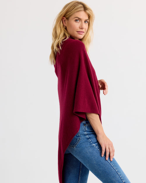 LIFESTYLE / EDITORIAL: Woman wearing barolo red cashmere poncho and blue jeans, posing sideways against white background